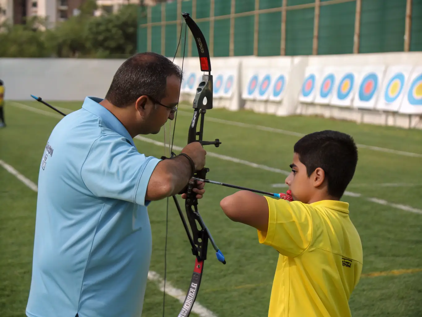 A photograph capturing a coach providing personalized archery technique guidance to a club member at Massilia Arc Club's training facility.